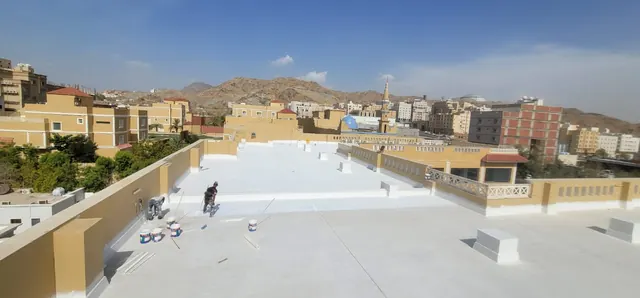 عاملان يطبقان طبقة عزل بيضاء على سطح مبنى